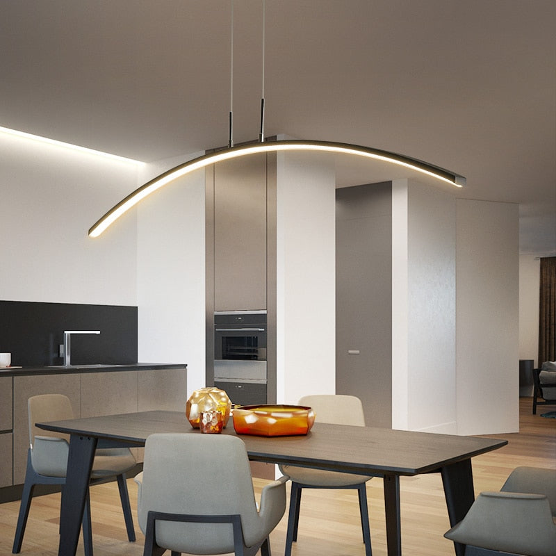 Modern LED pendant light with a curved design, installed over a dining table in a bright interior setting.